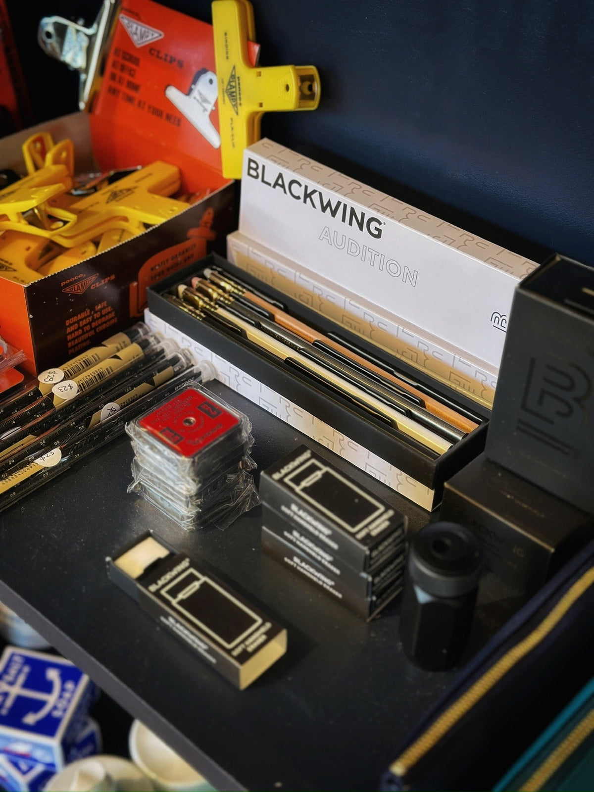 Blackwing pencils, erasers, Penco rulers and tape measures stacked neatly on a black surface