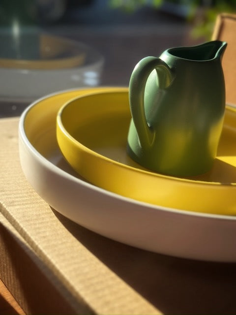 Green ceramic Jug, Yellow shallow bowl, cream platter from Bison Home, lit by sunlight in the Mill Room Mercantile window. 
