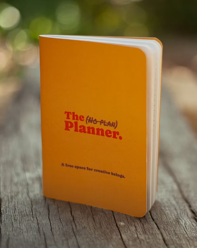 Turmeric Orange mini notebook titled 'The (No-Plan) Planner' on a wooden surface.